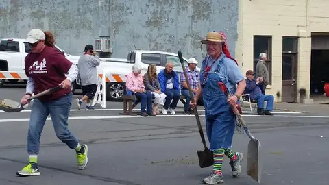 People dressed in costume holding shovels walk in the street during an event.