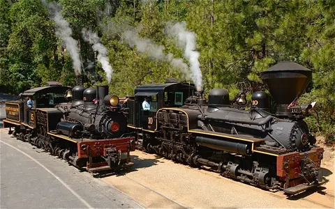Two steam locomotives parked outdoors on tracks next to trees.
