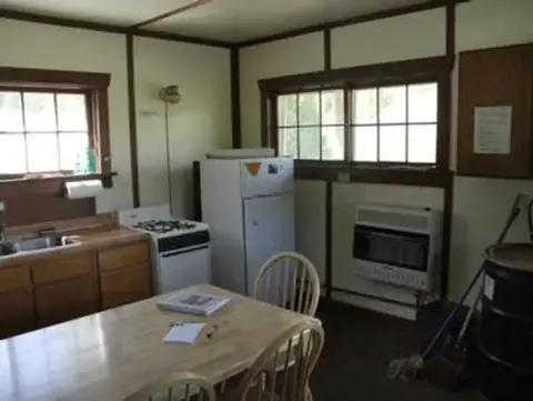An interior view of a rustic kitchen with a dining table, stove, and refrigerator.