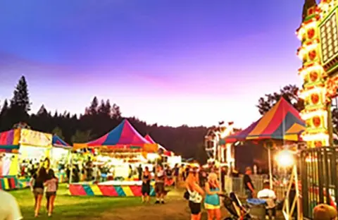 A colorful carnival at dusk with tents and people.