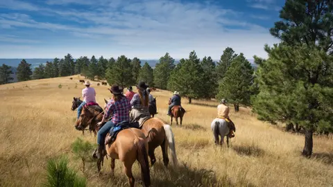 A group of people ride horses across a grassy hillside field.