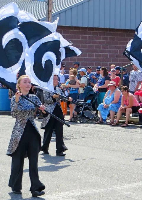 Performers in sparkly jackets carry black and white flags past a crowd.