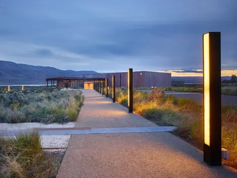 An illuminated path leads toward a building at dusk with mountains in the background.