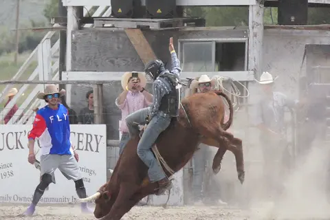 A cowboy rides a bucking bull at a rodeo arena.