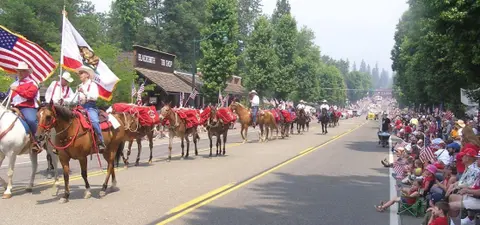 People riding horses and mules carrying flags down a street lined with spectators.