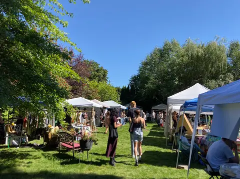 An outdoor market with tents and people gathered on a grassy lawn.