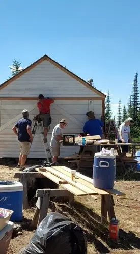 Several people working on the exterior of a small wooden building.
