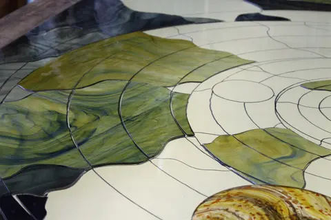 A close-up view of stained glass pieces being assembled on a light table.