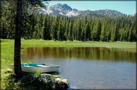 A small boat rests on the shore of a calm mountain lake.