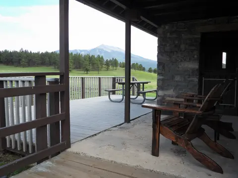A view from a porch with wooden chairs looking out towards a mountain and grassy landscape.
