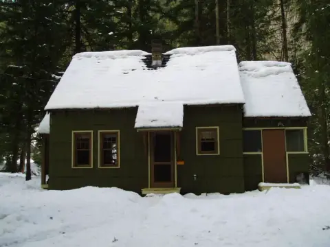 A small cabin covered in snow in a forest.