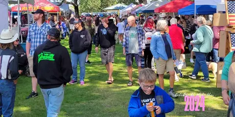 A crowd of people walks through an outdoor festival with tents and booths.