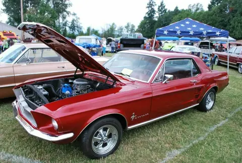 A red vintage car parked on grass at an outdoor event with its hood open.