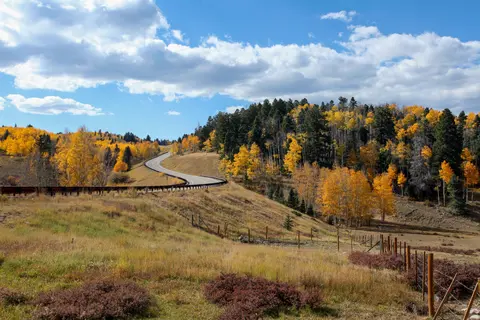 A winding road through a landscape with autumn foliage and a cloudy blue sky.