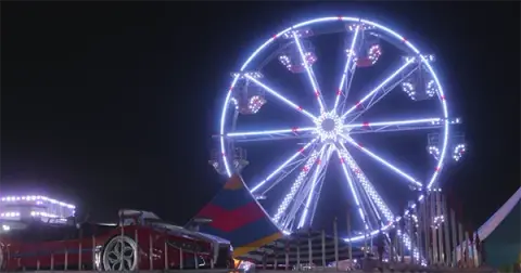 A brightly lit Ferris wheel at night at a carnival.