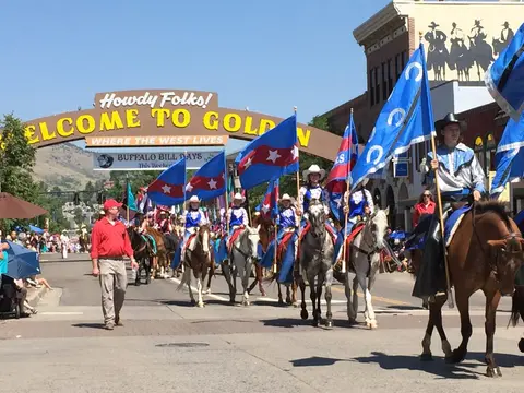 A parade featuring people riding horses with flags under an archway.