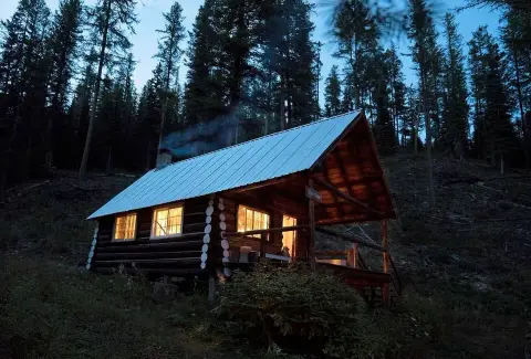 A rustic log cabin nestled among tall pine trees at twilight.