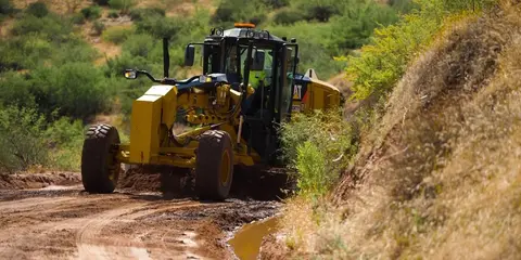 A yellow motor grader is operating on a dirt road.