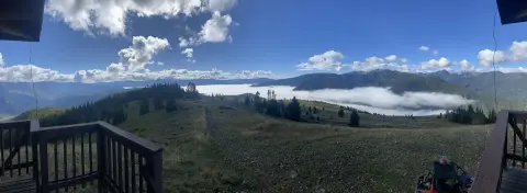 A panoramic view from a wooden deck overlooking mountains and low-lying clouds.