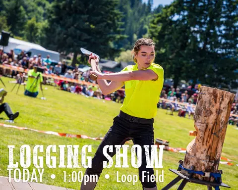 A woman chops a log with an axe at an outdoor logging show.