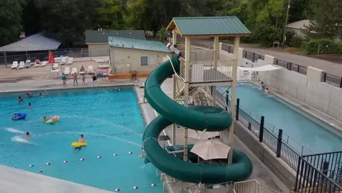 An outdoor swimming pool complex with a large green spiral slide.