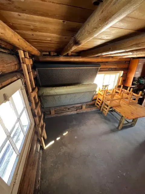 An interior view of a rustic log cabin with bunks and stacked chairs.
