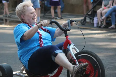 A smiling woman rides a small tricycle outdoors.