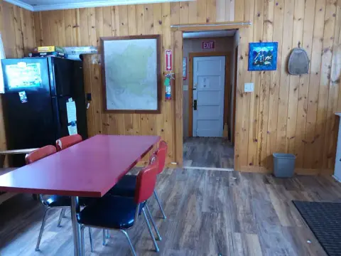 An interior room with wood-paneled walls, a red table with chairs, and a doorway.