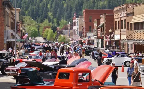 A street lined with historic brick buildings and classic cars parked on both sides during an event.