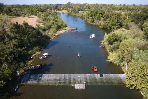 An aerial view of a river with several boats and a barrier structure.