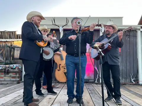 A band of musicians playing instruments outdoors on a wooden deck.