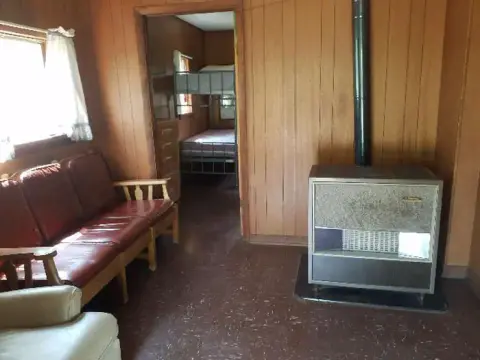 Interior view of a wood-paneled room with a sofa and heater, with a bedroom visible through a doorway.