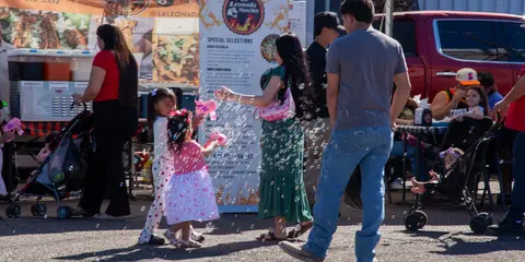People gather near an outdoor food stand while children play with bubble blowers.