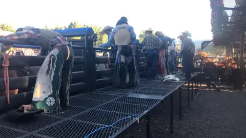Cowboys stand on a metal platform near rodeo chutes.