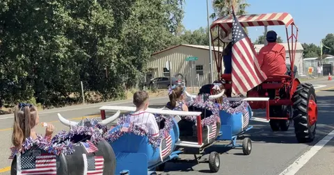 A decorated train made of barrels is pulled by a tractor along a road in a parade.