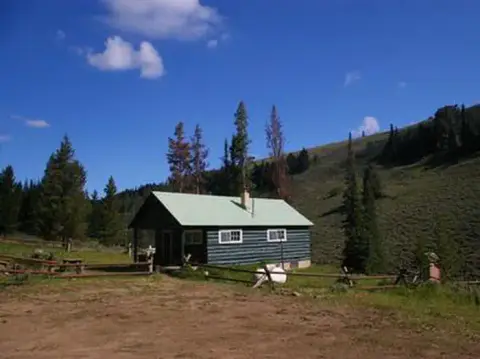 A cabin nestled in a mountainous landscape under a blue sky.
