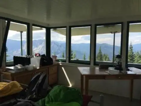 Interior view of a lookout cabin with panoramic windows overlooking a mountain range.