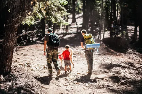 Two adults and a child hike along a wooded dirt trail.