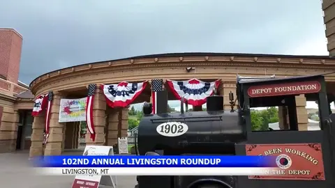 A steam locomotive replica parked outside a brick building decorated with patriotic bunting.