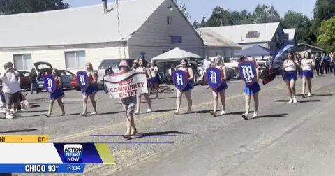 A marching band and community entry participants walk down a street during a parade.