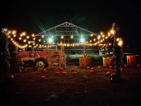 A nighttime view of a decorated farm building with pumpkins and string lights.