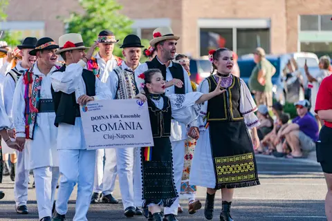 A group of people in traditional folk attire walking in a parade holding a sign.