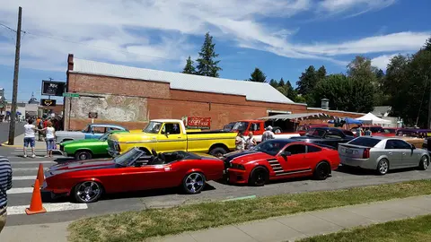 A street lined with classic and modern cars parked along a brick building.