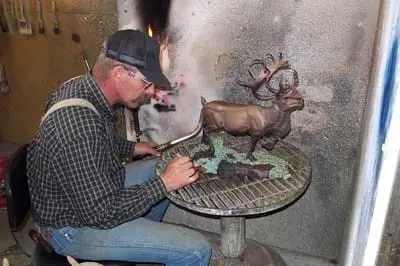 A man works on a sculpture of a deer in a workshop.