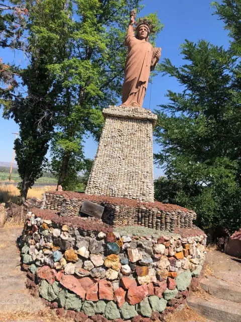 A statue of the Statue of Liberty on a stone pedestal surrounded by trees.