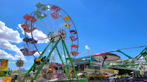 A colorful Ferris wheel stands against a blue sky with white clouds at a fair.
