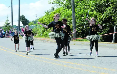 Children marching in a parade while twirling batons on a street.