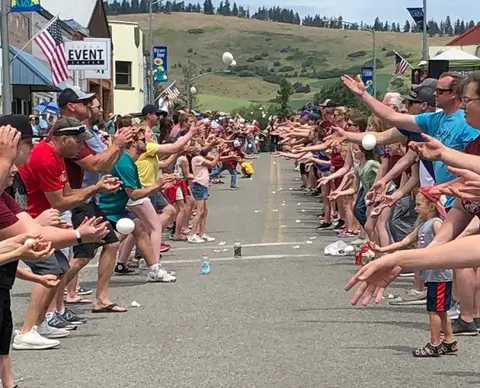 People stand in two lines on a street participating in an egg toss event.