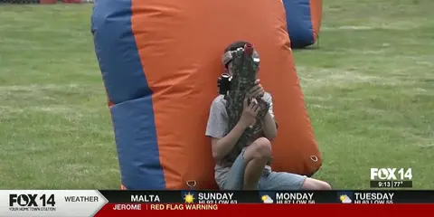 A young person playing laser tag near an inflatable barrier on a grassy field.