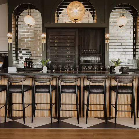 A stylish bar interior with dark wood, tiled arches, and several stools lined up along the counter.